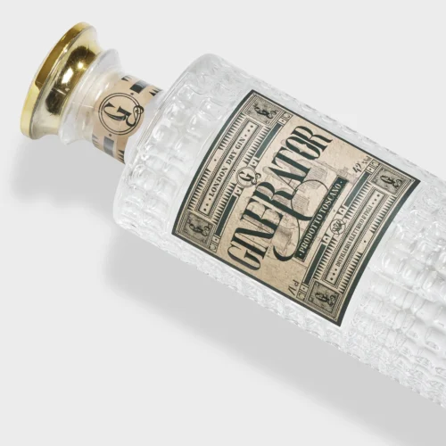 En tekstureret glasflaske med en guldhætte mærket "Ginerator London Dry Gin 42% 70cl" med fed skrift på en vintage cremefarvet og grøn etiket, sat mod en lys baggrund.